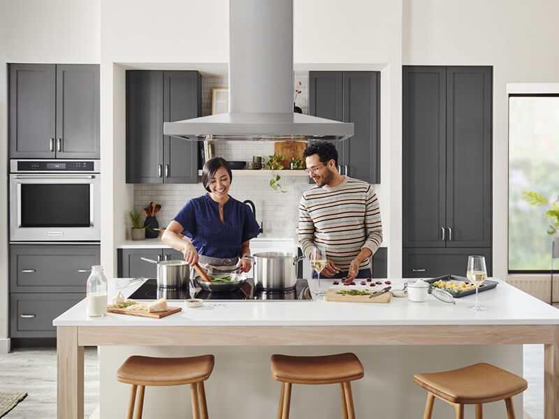 Two people cooking at a kitchen island over a cooktop Two people cooking at a kitchen island over a cooktop