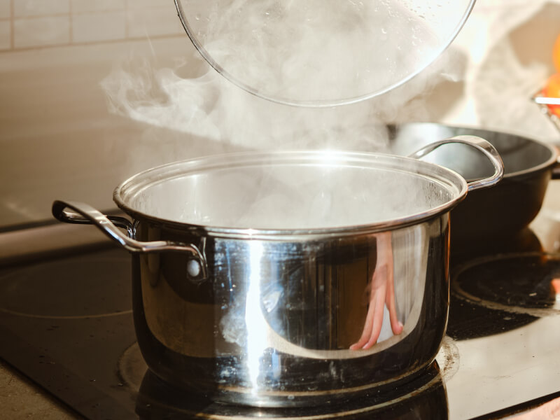 Someone lifting a lid off of a steaming pot