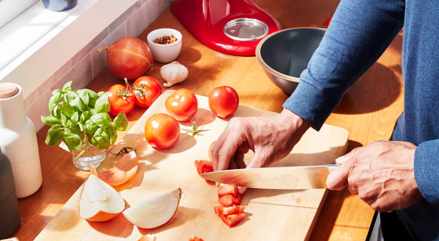 A person chopping tomatoes and onions at their countertop