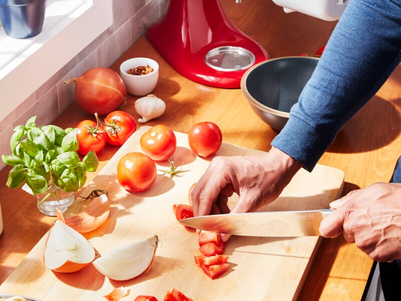 A person chopping tomatoes and onions at their countertop
