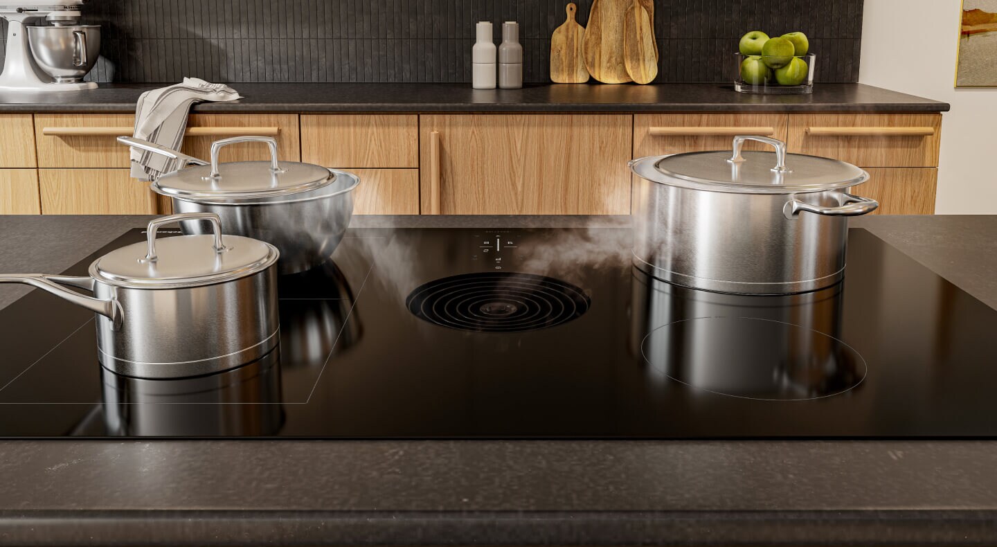 A KitchenAid® induction downdraft cooktop with several pots cooking food
