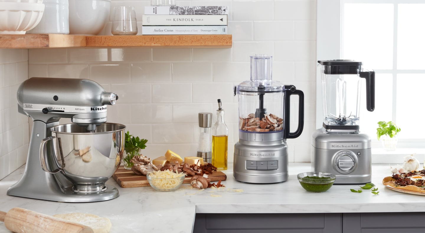 Silver KitchenAid® stand mixer, food processor and blender on counter next to prepared ingredients Silver KitchenAid® stand mixer, food processor and blender on counter next to prepared ingredients