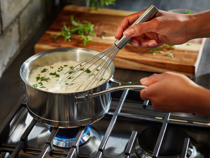 Person whisking soup on a gas stovetop