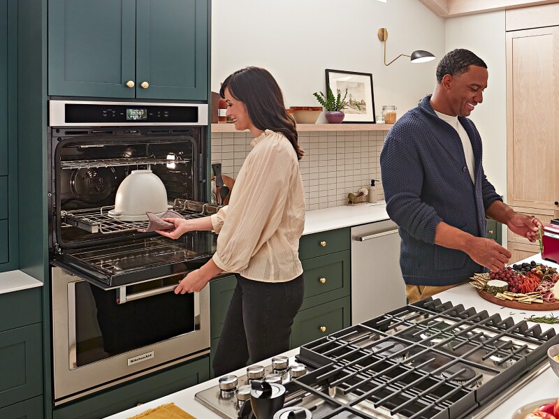 People gathered around a kitchen island while person removes dish from KitchenAid® double wall oven People gathered around a kitchen island while person removes dish from KitchenAid® double wall oven
