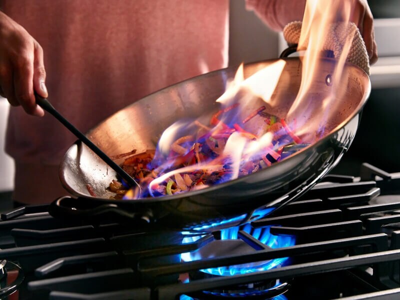 Someone flambeing food in a pan on a cooktop