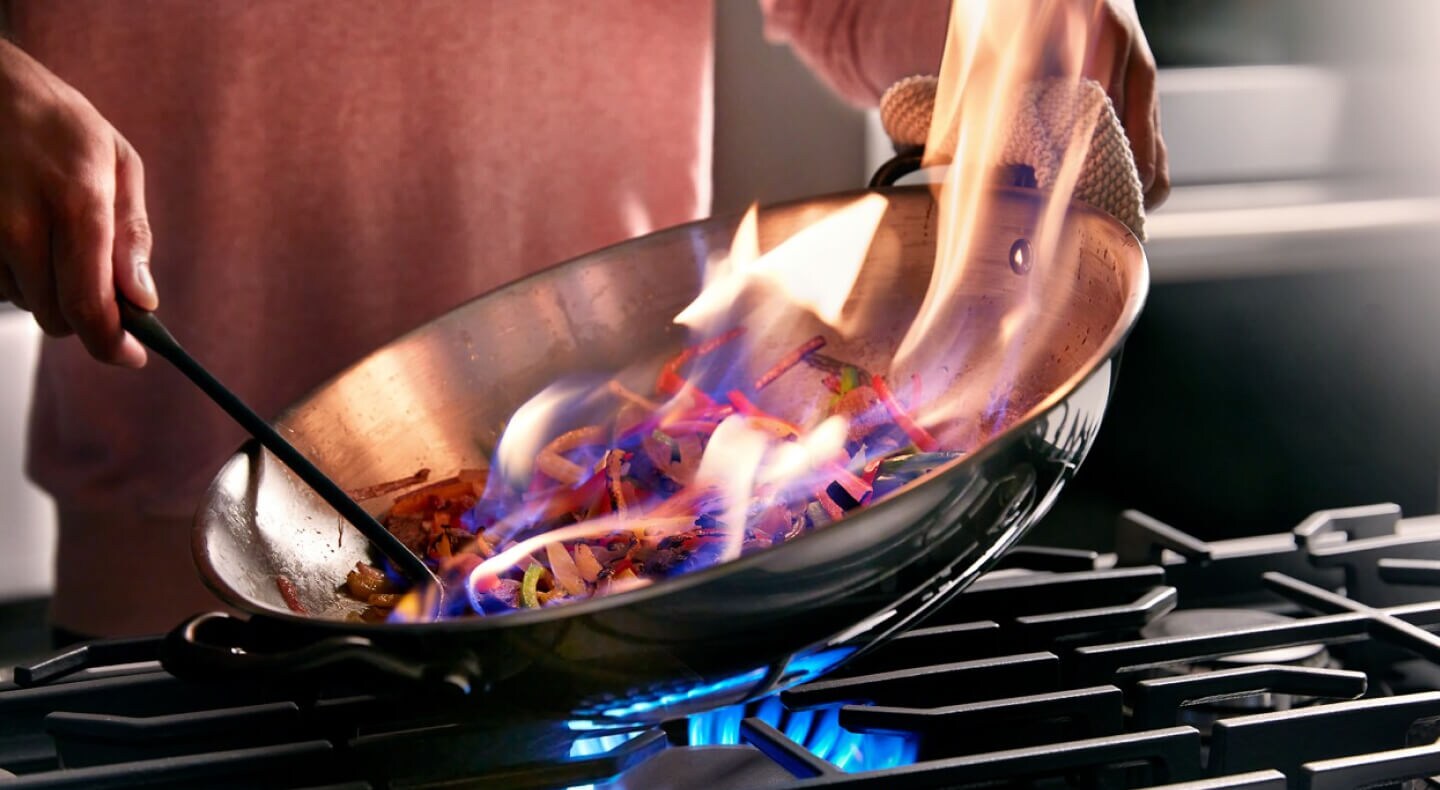 Someone flambeing food in a pan on a cooktop