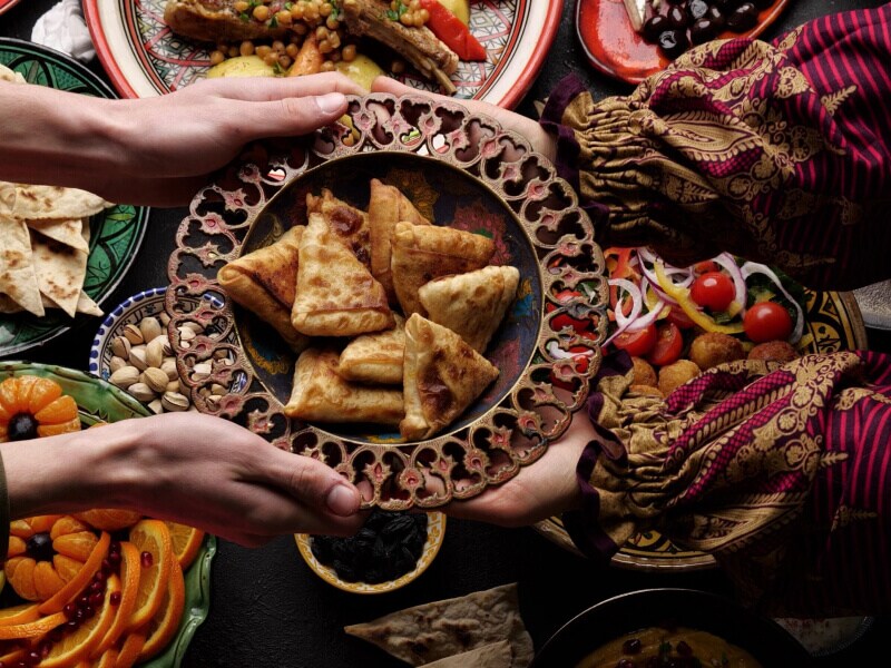A person passing a bowl of food over an array of ethnic dishes in colorful display