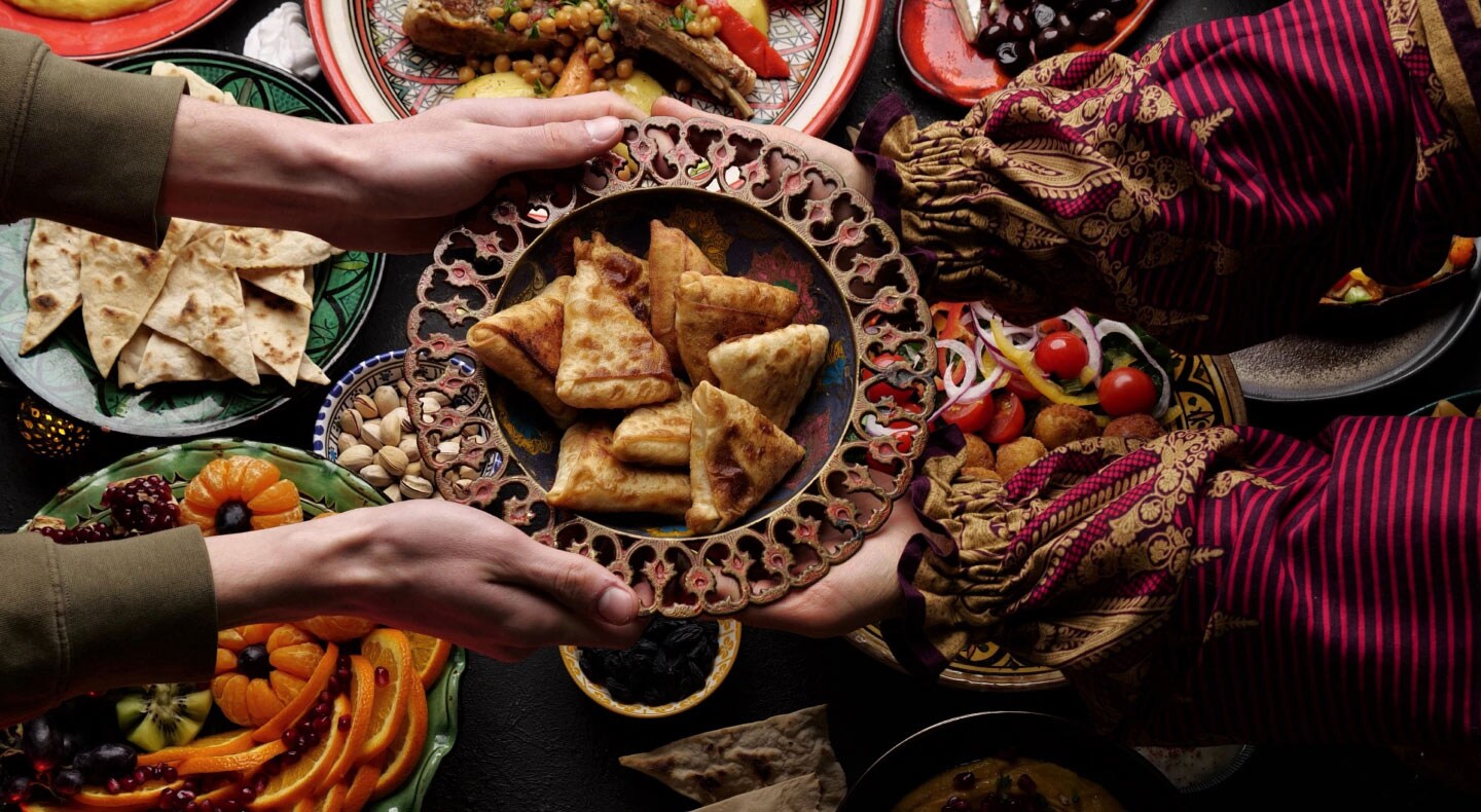 A person passing a bowl of food over an array of ethnic dishes in colorful display