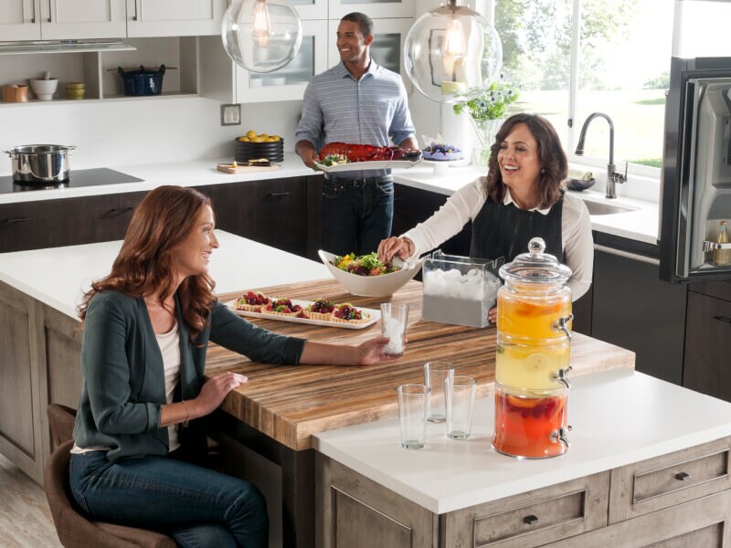 People gathering in a kitchen around an island and sharing food and drink