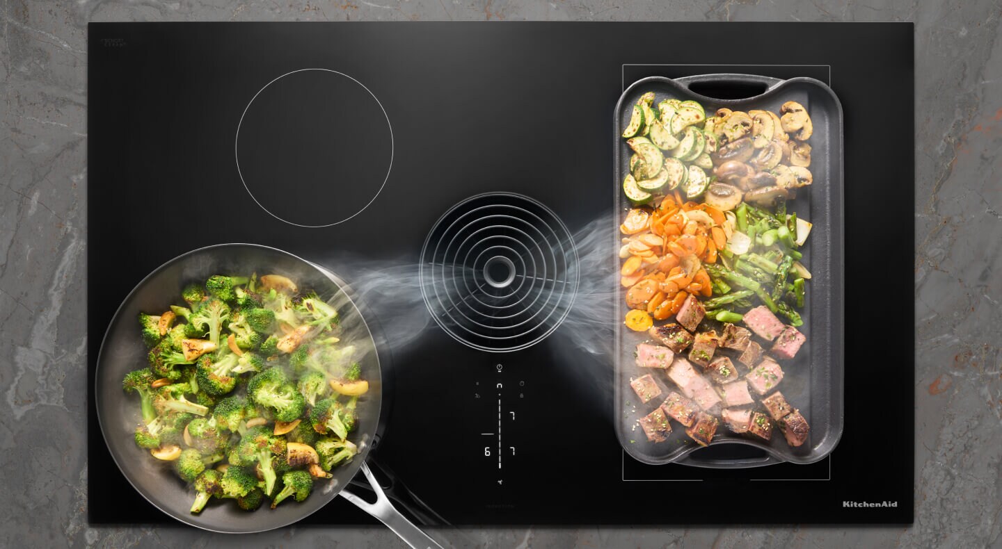 Various dishes cooking on a cooktop with downdraft ventilation