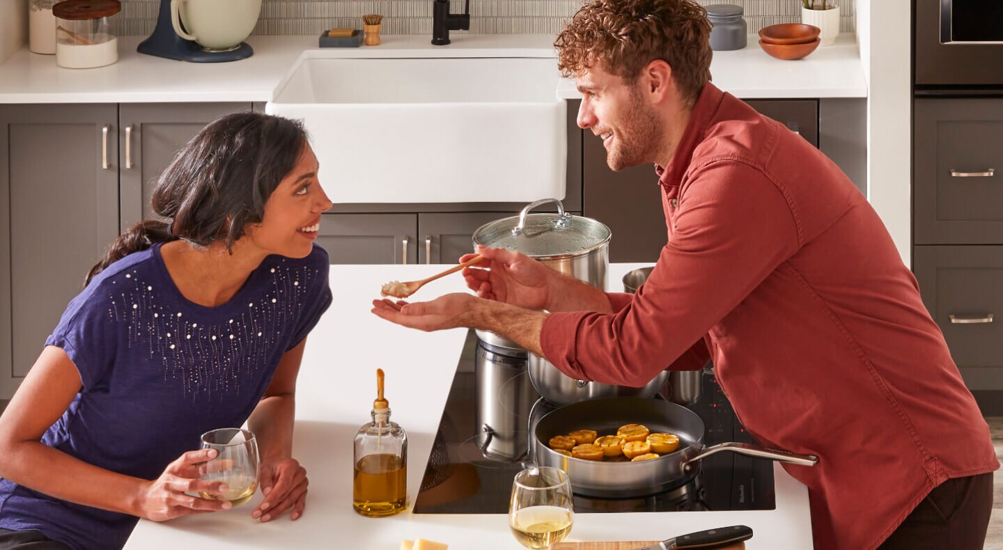 A man and a woman cooking and tasting food together at a kitchen island