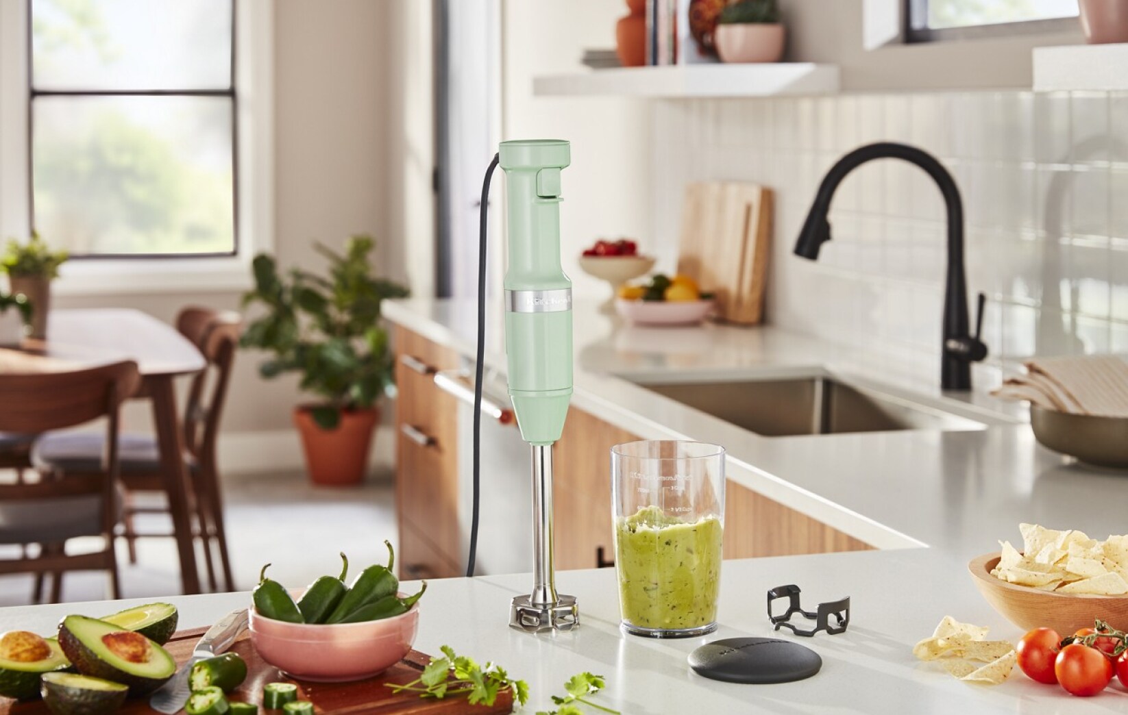 A Variable Speed Corded Hand Blender on a counter with guacamole ingredients and guacamole in the blender jar.
