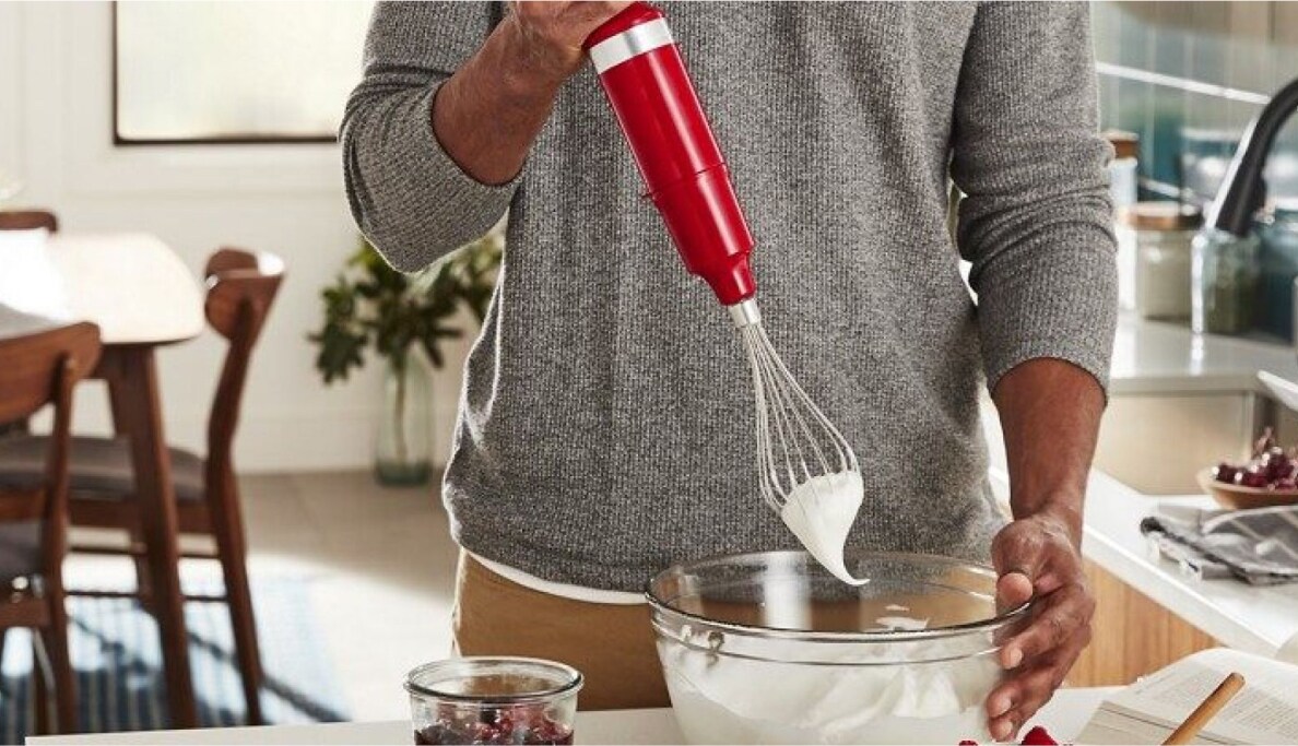A peson using a hand blender to whip cream.
