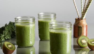 Green smoothies in jars surrounded by kiwis.