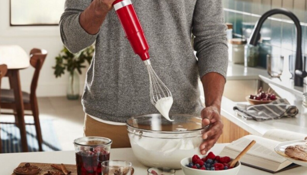A person whipping cream with an immersion blender and whisk accessory.