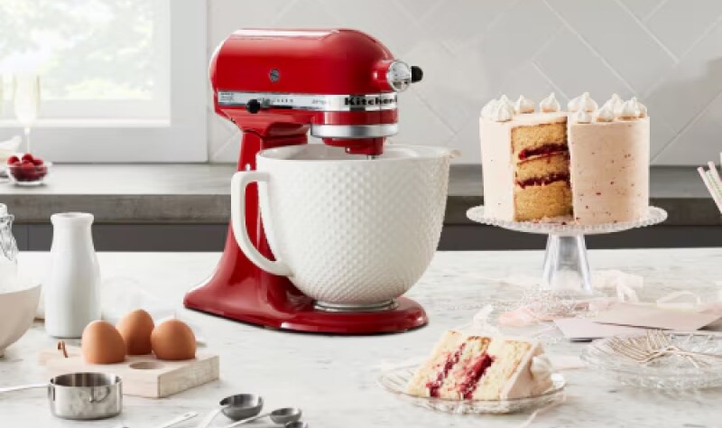 A red KitchenAid standmixer with a cake on a stand nearby