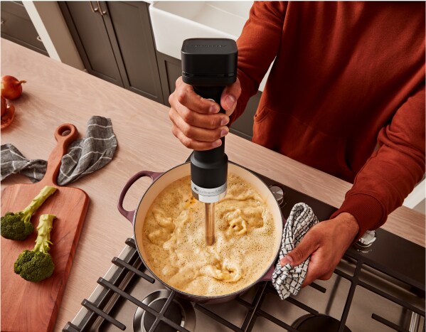 A person using a KitchenAid Go™ Cordless Hand Blender in a dutch oven of soup