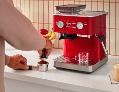A person tamping down coffee grounds in front of a KitchenAid Espresso Machine