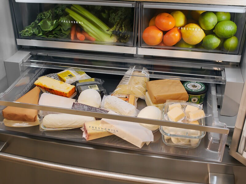 A refrigerator with an open drawer full of various cheeses