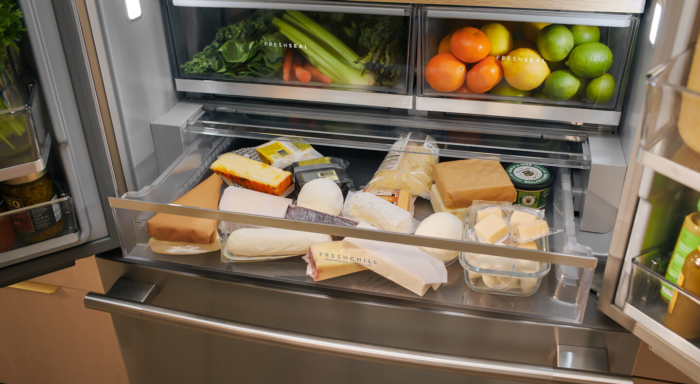 A refrigerator with an open drawer full of various cheeses