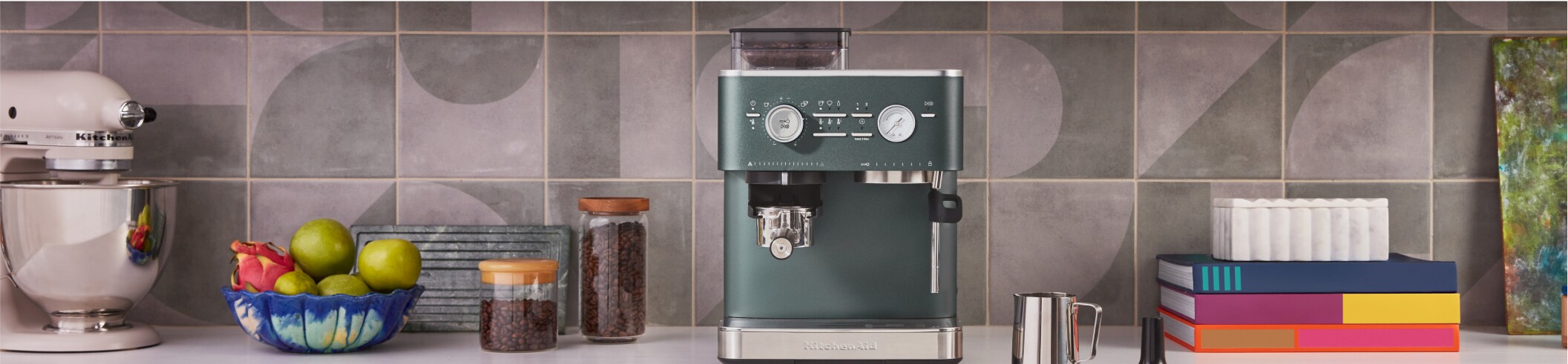 A KitchenAid® espresso machine in juniper, with a person tamping down espresso grounds.