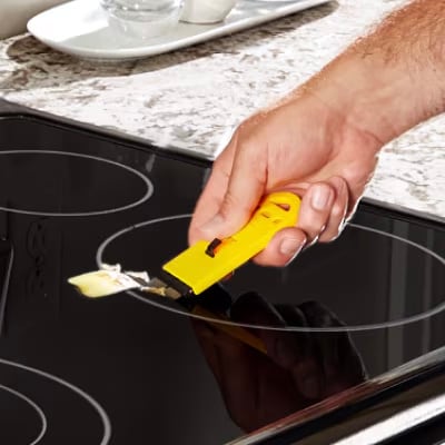Hand using a scraper to clean an induction cooktop