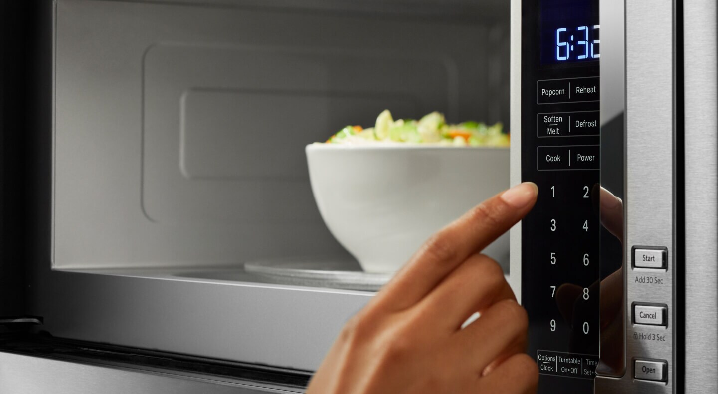 Close-up of person selecting settings on a KitchenAid® microwave with hidden controls