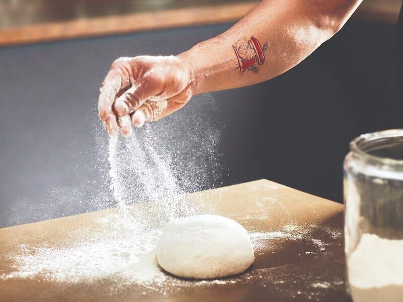 Person sprinkling flour over a ball of dough