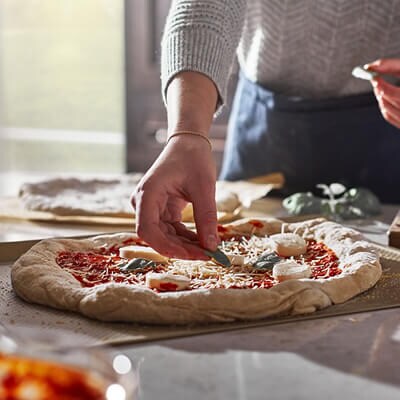 Someone putting ingredients on a pizza