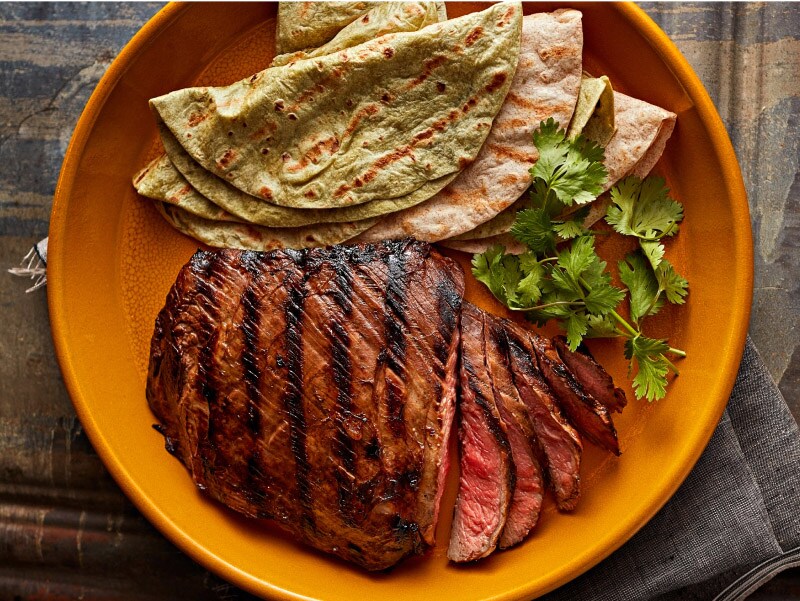 Grilled flat iron steak with green and yellow tortillas on the side