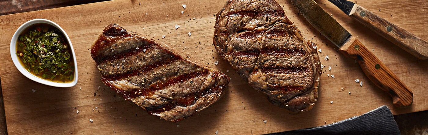 Steak resting on a cutting board next to a bowl of chimichurri sauce