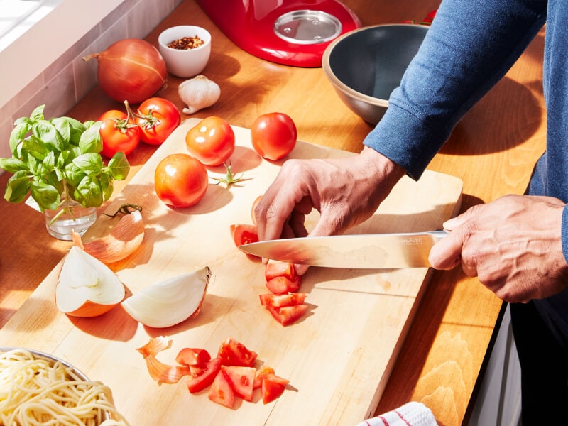 A person chopping tomatoes on a cutting board A person chopping tomatoes on a cutting board