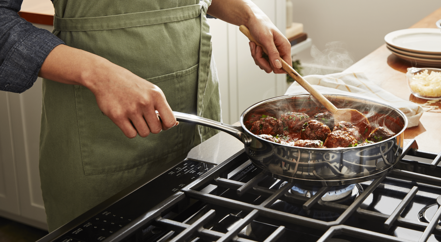 A person simmering vegan "meatballs" on a stovetop A person simmering vegan "meatballs" on a stovetop