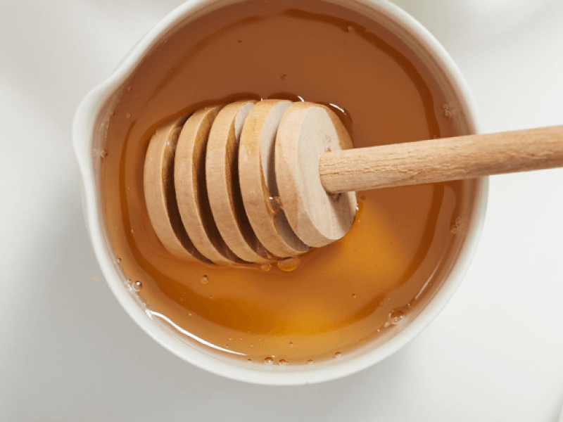 A honey dipper placed inside a bowl of vegan honey A honey dipper placed inside a bowl of vegan honey