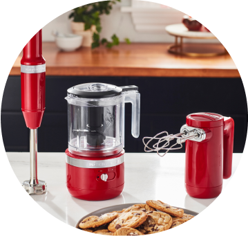 Empire Red KitchenAid® Cordless Immersion Blender, Food Chopper, and Hand Mixer on white countertop.