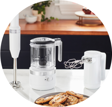 White KitchenAid® Cordless Immersion Blender, Food Chopper, and Hand Mixer on white countertop.