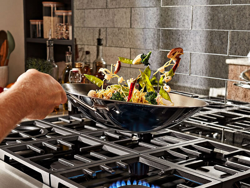 Person flipping stirfry in a wok over a gas stove