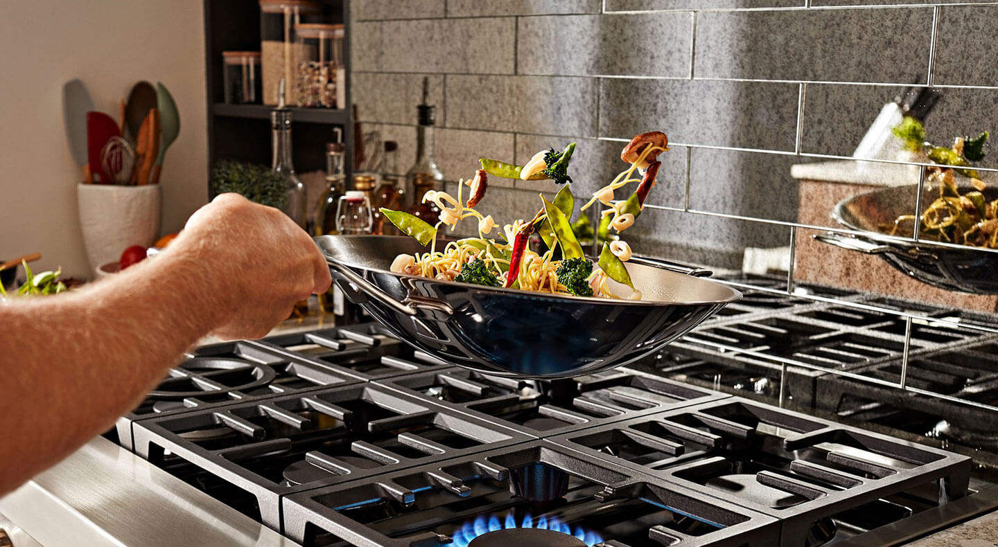 Person flipping stirfry in a wok over a gas stove