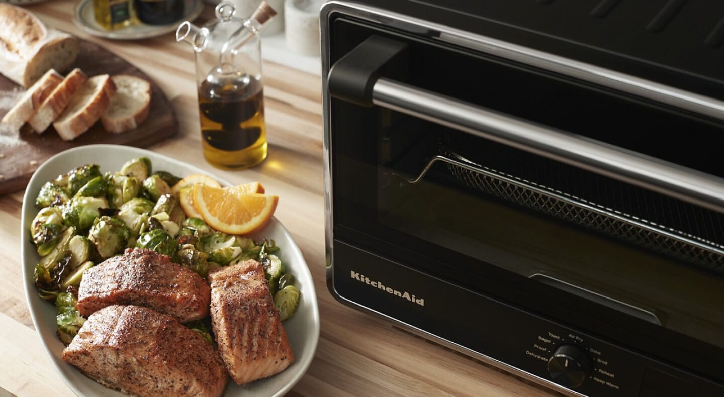 Air fried salmon and Brussels sprouts next to a KitchenAid® countertop oven
