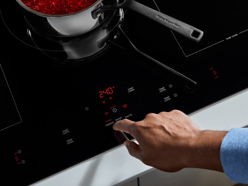 A finger selecting a KitchenAid® induction cooktop feature
