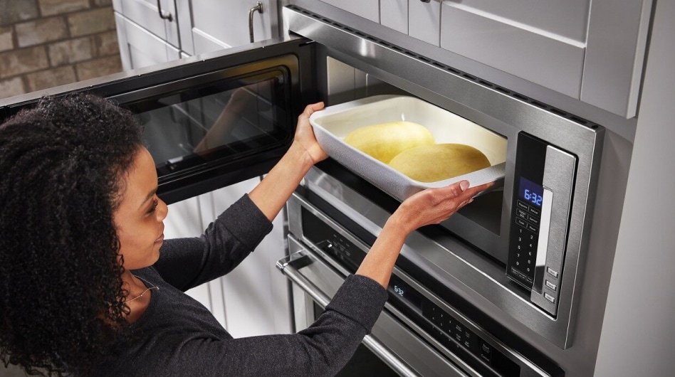 A person placing a dish with loaves of dough into a microwave to proof A person placing a dish with loaves of dough into a microwave to proof