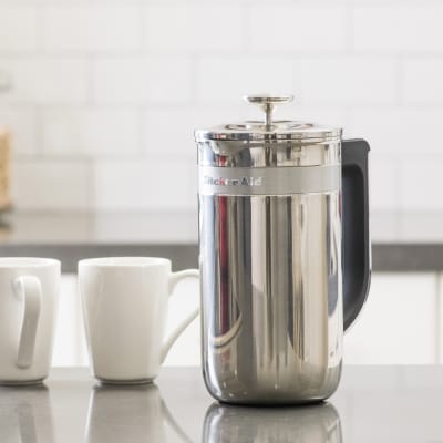 French press coffee maker next to two mugs