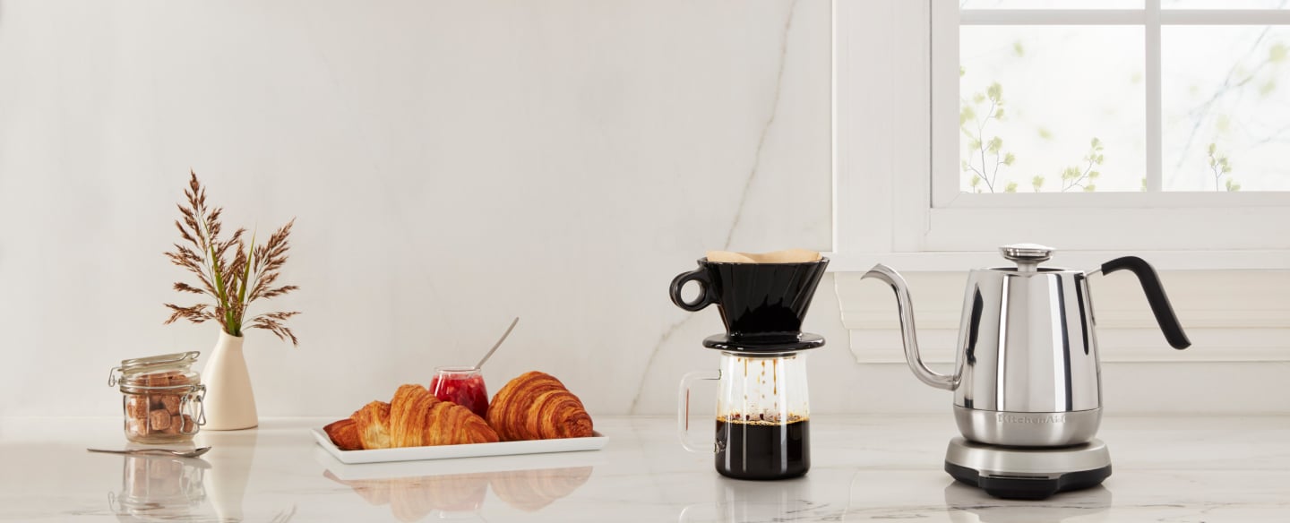 Same as Image Alt Text KitchenAid® electric goose-necked kettle next to a coffee and pastries