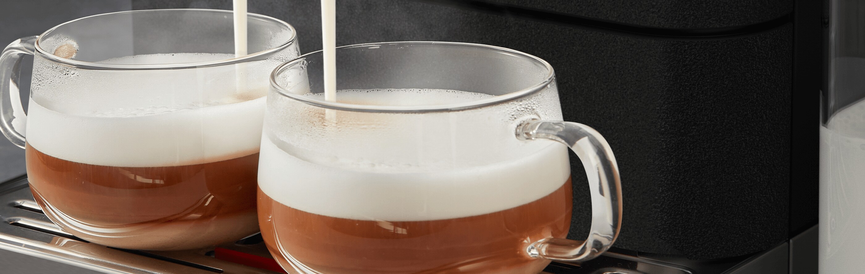 Glass mugs beneath an espresso machine being filled with frothed milk