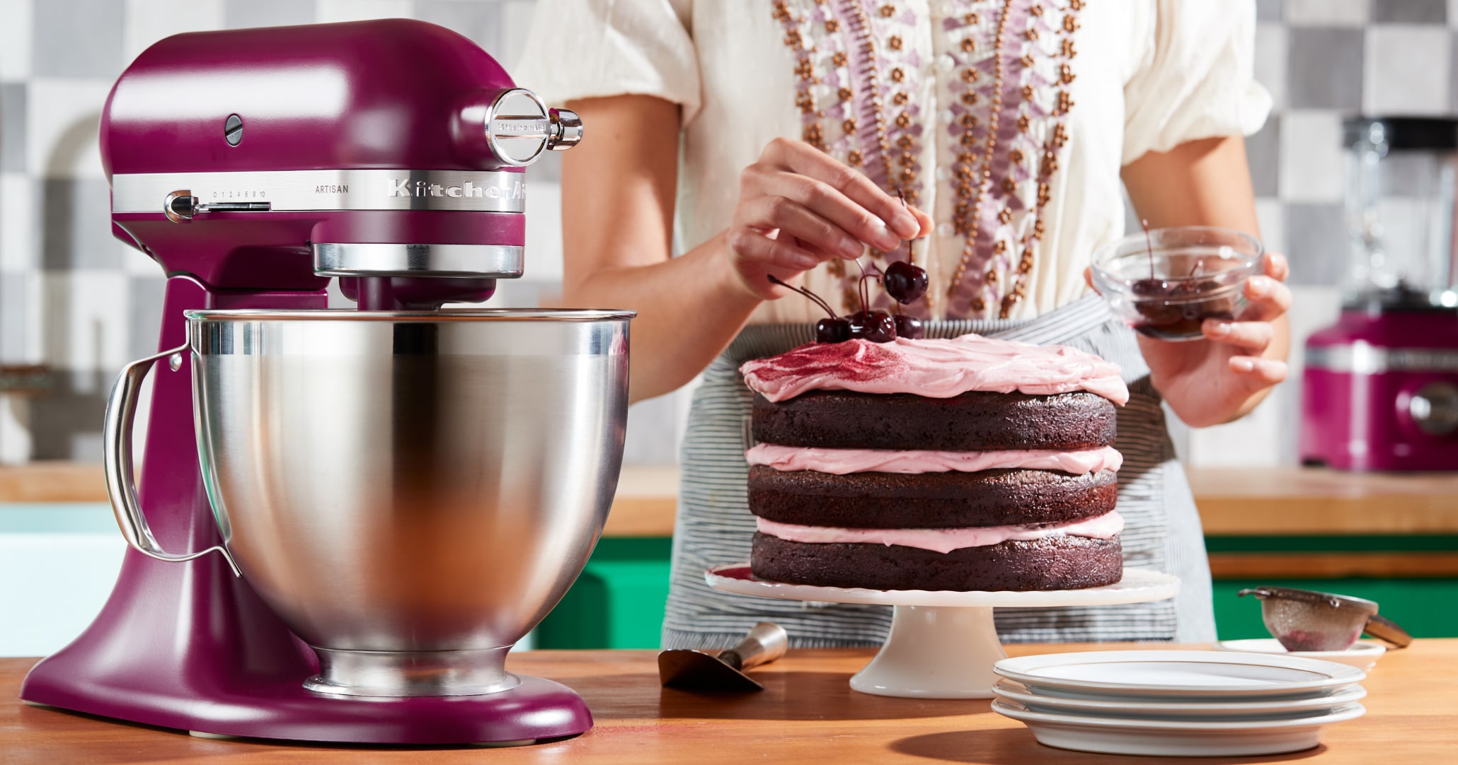 Woman garnishing chocolate layer cake with cherries placed next to KitchenAid® stand mixer in Beetroot Woman garnishing chocolate layer cake with cherries placed next to KitchenAid® stand mixer in Beetroot