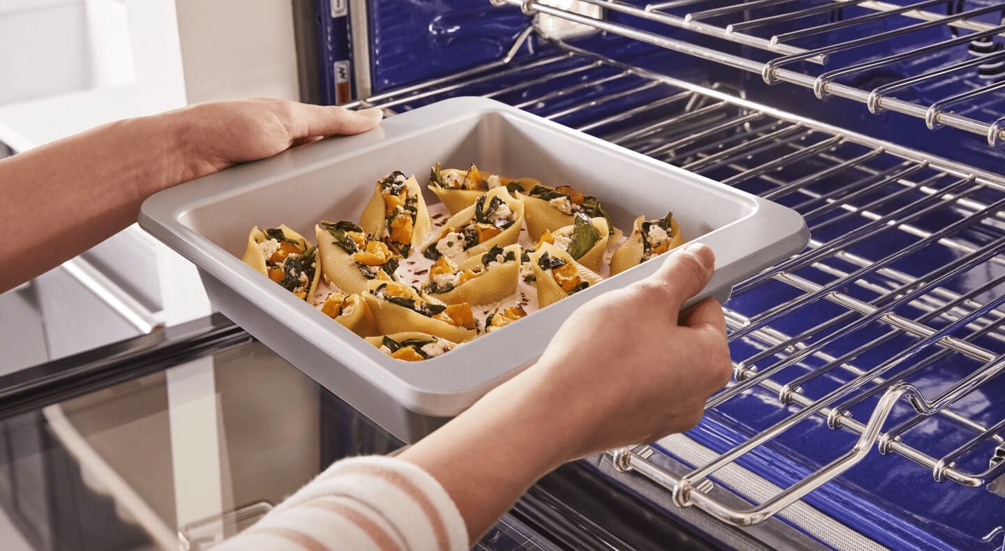 A person placing a tray of stuffed shells on the lower rack of a convection oven A person placing a tray of stuffed shells on the lower rack of a convection oven