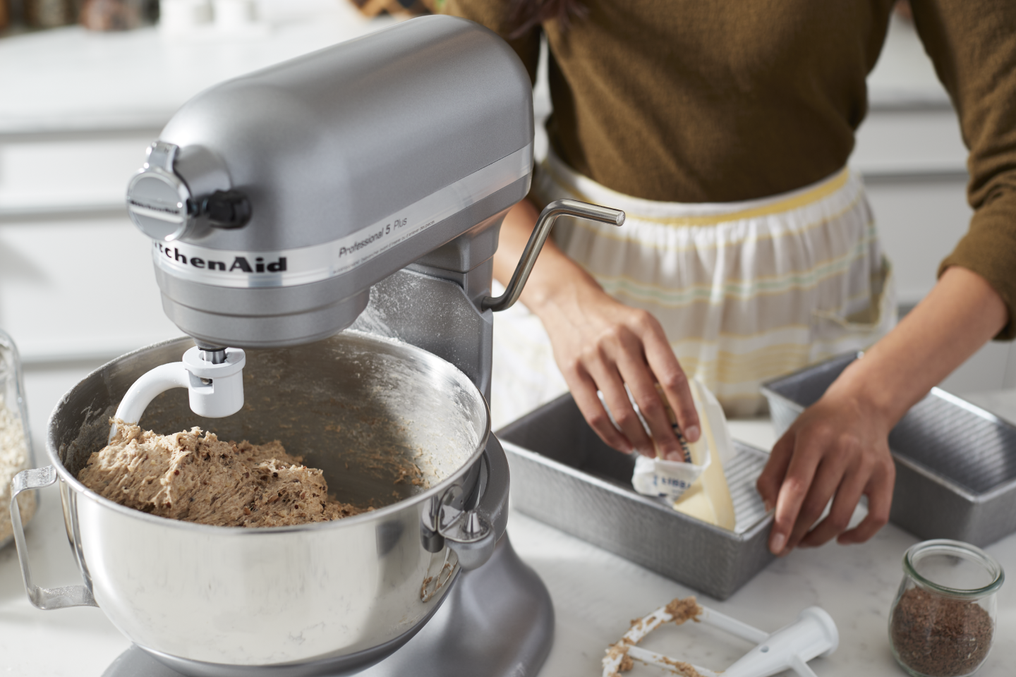 A person using a silver KitchenAid® stand mixer. A person using a silver KitchenAid® stand mixer.