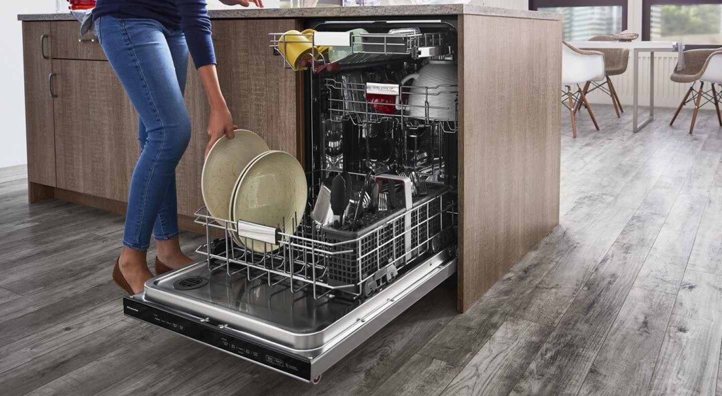 A closeup of a person loading plates onto the bottom rack of a stainless steel KitchenAid® dishwasher. A closeup of a person loading plates onto the bottom rack of a stainless steel KitchenAid® dishwasher.