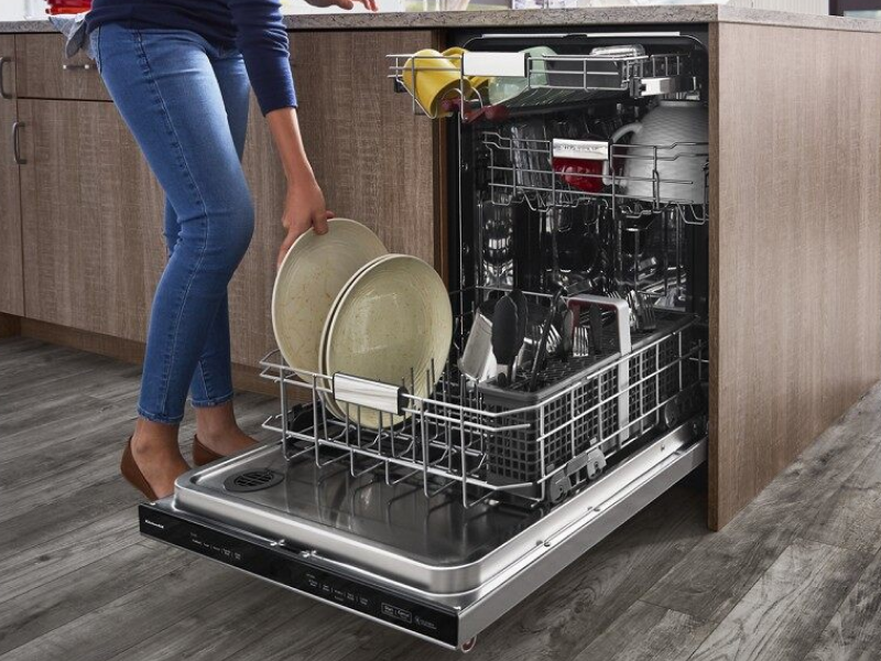 A closeup of a person loading plates onto the bottom rack of a stainless steel KitchenAid® dishwasher. A closeup of a person loading plates onto the bottom rack of a stainless steel KitchenAid® dishwasher.
