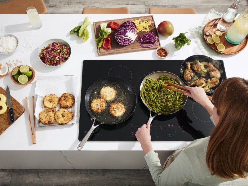 Person sauteeing green beans on electric cooktop surrounded by ingredients Person sauteeing green beans on electric cooktop surrounded by ingredients